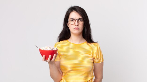 Jolie femme se sentant triste, bouleversée ou en colère et regardant sur le côté et tenant un bol de petit-déjeuner