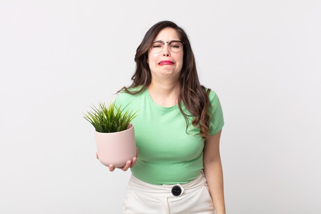 Jolie femme se sentant triste et pleurnicharde avec un regard malheureux et pleurant et tenant une plante décorative