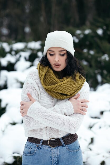 Jolie femme se tenir à l'extérieur du parc à neige street hiver météo forêt vêtue d'un pull chaud tricoté et s