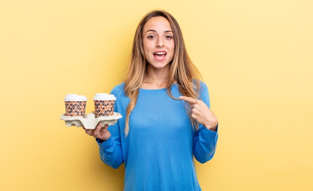 Jolie femme semblant choquée et surprise avec la bouche grande ouverte, pointant vers soi. concept de café à emporter