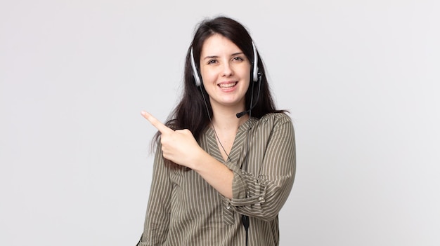 Jolie femme semblant excitée et surprise en pointant sur le côté. agent assistant avec un casque