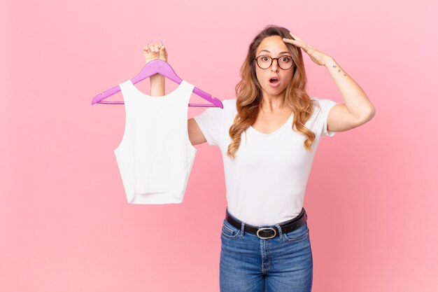 Jolie femme semblant heureuse, étonnée et surprise et choisissant des vêtements