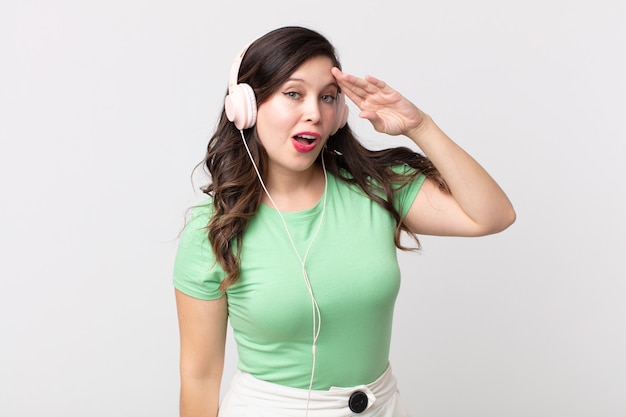 Jolie femme semblant heureuse, étonnée et surprise d'écouter de la musique avec des écouteurs