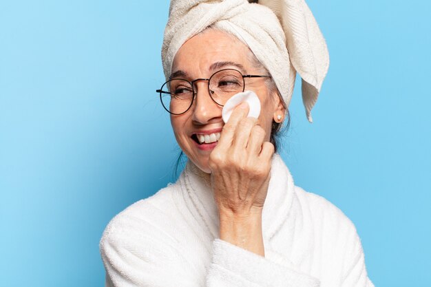 Jolie femme senior nettoyage du visage ou maquillage après la douche portant un peignoir