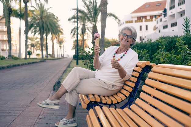 Jolie femme senior souriante et heureuse appréciant un cornet de crème glacée assis sur un banc jaune