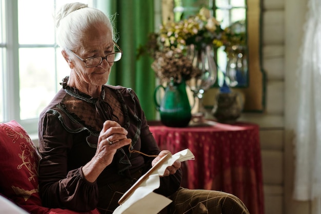 Jolie femme senior avec toile en cerceau au point de croix dans le salon