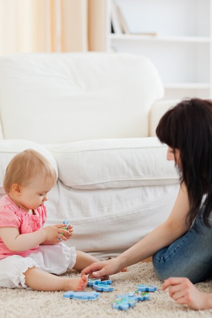 Jolie femme et son bébé jouant avec des pièces de puzzle tout en étant assis sur un tapis