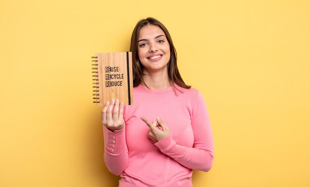 Jolie femme souriant joyeusement se sentant heureuse et pointant vers le concept de recyclage latéral