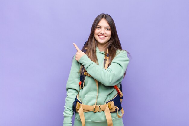 Jolie femme souriant joyeusement, se sentant heureuse et pointant vers le côté et vers le haut, montrant l'objet dans l'espace de copie