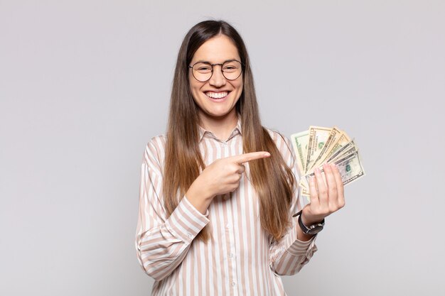 Jolie femme souriant joyeusement, se sentant heureuse et pointant vers le côté et vers le haut, montrant l'objet dans l'espace de copie