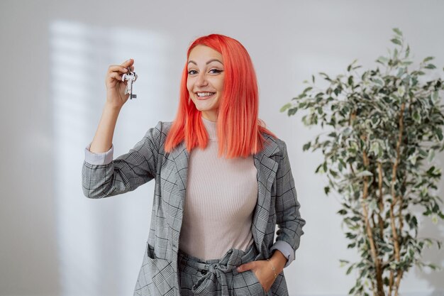 Une jolie femme souriante aux cheveux roses vêtue d'un costume à carreaux intelligent détient les clés d'un appartement i