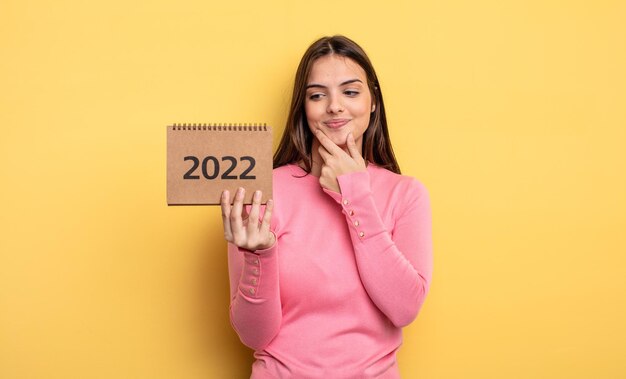 Jolie femme souriante avec une expression heureuse et confiante avec la main sur le menton. Notion de calendrier 2022