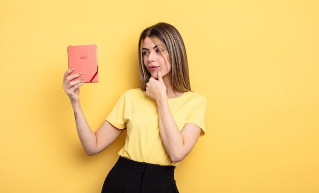 jolie femme souriante avec une expression heureuse et confiante avec la main sur le menton. notion de planificateur