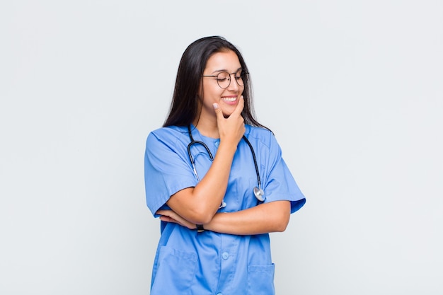 Jolie femme souriante avec une expression heureuse et confiante avec la main sur le menton, se demandant et regardant sur le côté