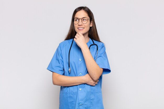 Jolie femme souriante avec une expression heureuse et confiante avec la main sur le menton, se demandant et regardant sur le côté