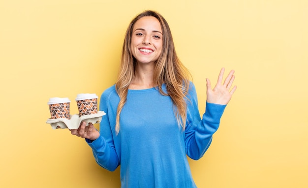 Jolie femme souriante joyeusement, agitant la main, vous accueillant et vous saluant. concept de café à emporter