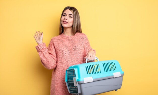 Jolie femme souriante joyeusement, agitant la main, vous accueillant et vous saluant. concept de transporteur pour animaux de compagnie