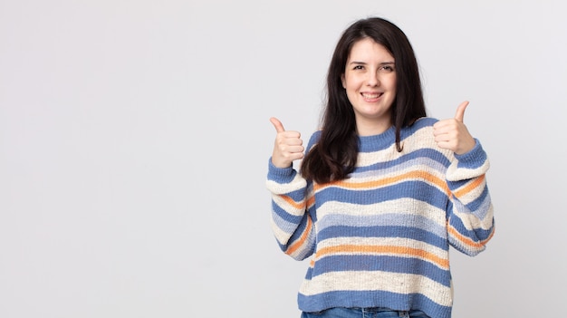 Jolie femme souriante joyeusement et ayant l'air heureuse, se sentant insouciante et positive avec les deux pouces vers le haut