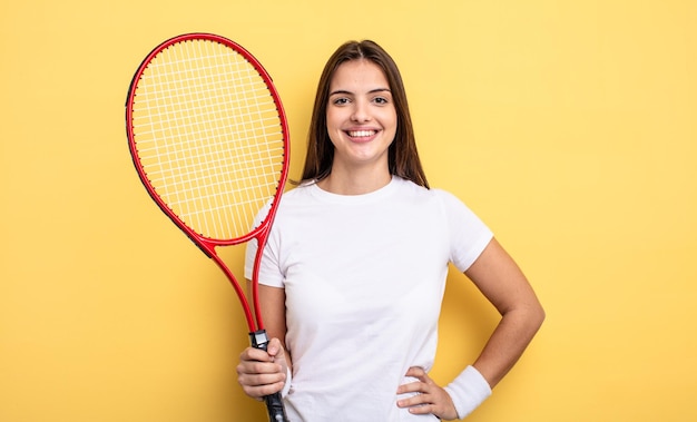 Jolie femme souriante joyeusement avec une main sur la hanche et confiante. concept de joueur de tennis