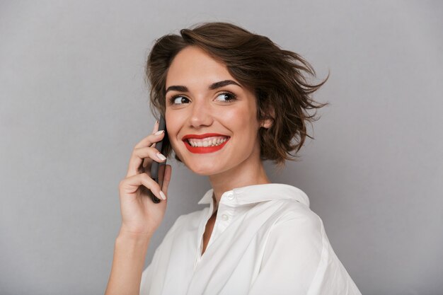 Jolie femme souriante et parlant au téléphone mobile, isolé sur mur gris