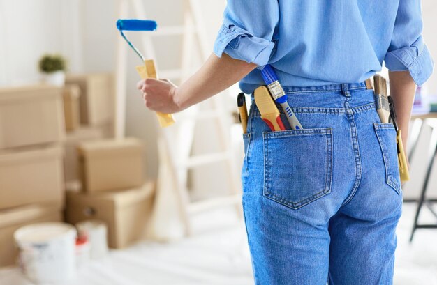 Jolie femme souriante peignant le mur intérieur de la maison avec un rouleau à peinture