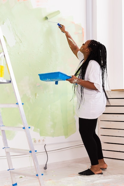 Photo jolie femme souriante peinture mur intérieur de la maison avec rouleau à peinture