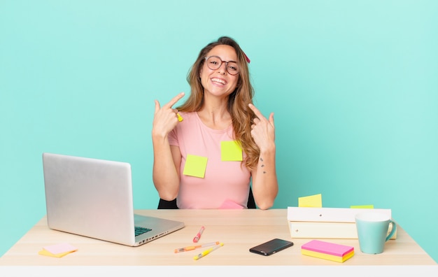 Jolie femme souriante pointant avec confiance vers son propre large sourire. concept de télétravail