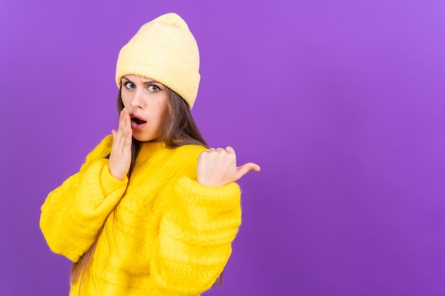 Jolie femme souriante pointant du doigt l'espace de copie sur un pull en laine de fond violet