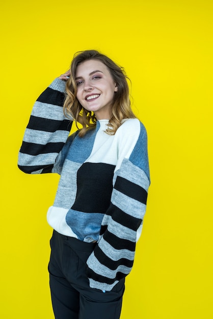 Jolie femme souriante posant en portant un pull tricoté isolé sur jaune