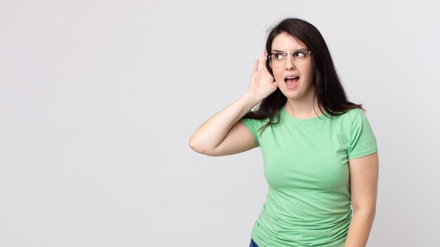 Jolie femme souriante, regardant curieusement sur le côté, essayant d'écouter des potins ou d'entendre un secret