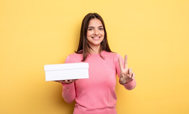 Jolie femme souriante et semblant heureuse, gestant la victoire ou la paix. concept d'emballage de boîte blanche