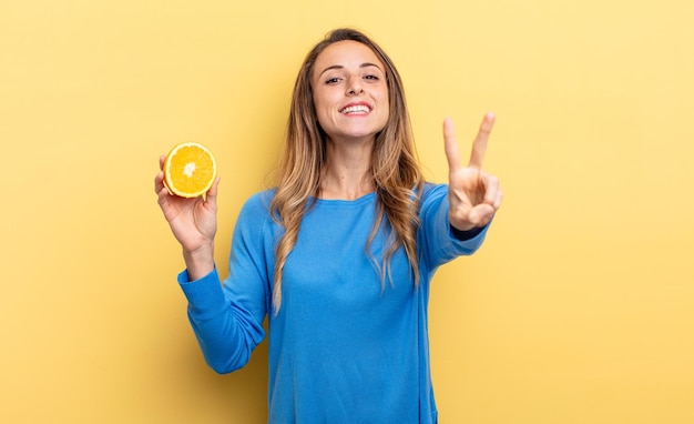 Jolie femme souriante et semblant heureuse, gesticulant victoire ou paix tenant une demi-orange