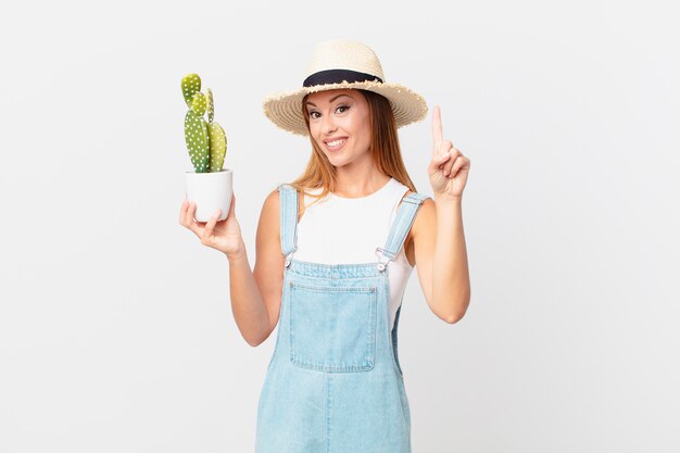 Jolie femme souriante et sympathique, montrant le numéro un et tenant une plante décorative de cactus