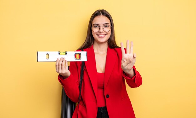 Jolie femme souriante et sympathique, montrant le numéro trois. architecte avec un niveau