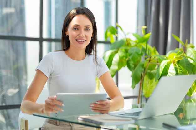 Jolie femme souriante travaillant sur une tablette dans un bureau moderne