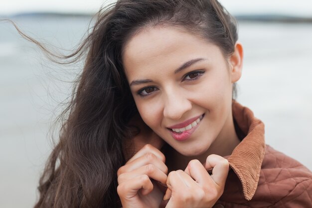 Jolie femme souriante en veste marron élégante sur la plage