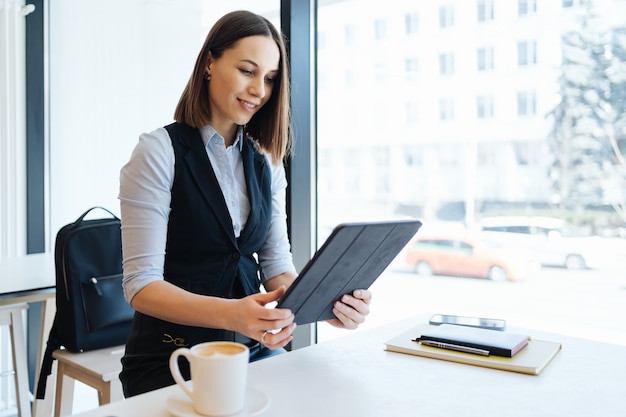 Jolie femme avec un sourire mignon prenant un café tout en vous relaxant dans une pause avec une tablette numérique