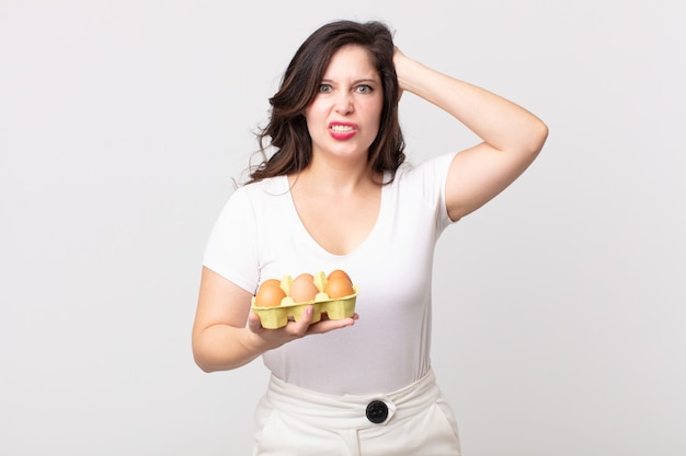 Jolie femme stressée, anxieuse ou effrayée, les mains sur la tête et tenant une boîte à œufs