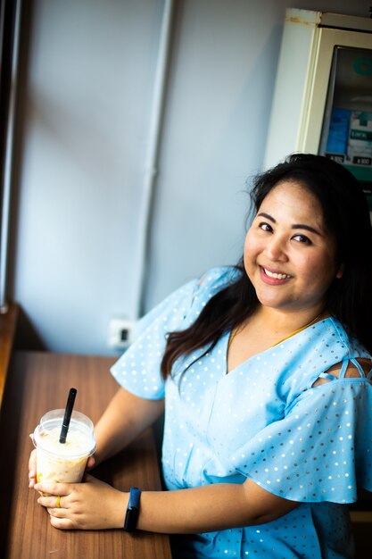 Jolie femme en surpoids dans un café-café, Heureuse femme asiatique dans un café avec une tasse de café en plastique