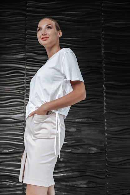 Jolie femme en T-shirt blanc et jupe au milieu d'un mur de bureau élégant noir