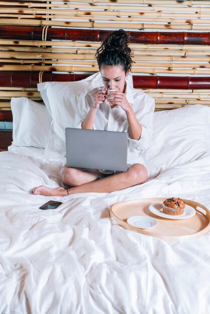 Jolie femme avec téléphone et ordinateur portable au lit