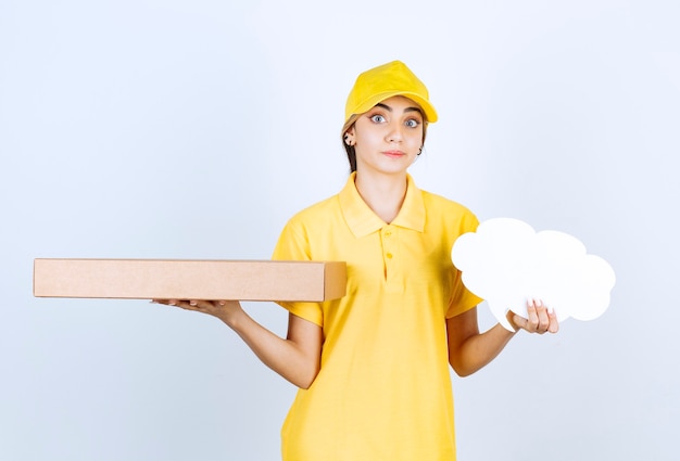 Une jolie femme tenant une boîte de papier kraft vierge marron et une bulle de dialogue vierge.