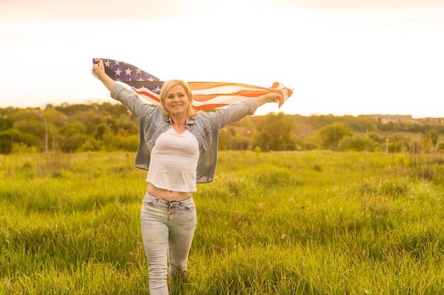 jolie femme tenant un drapeau américain dans le vent dans un champ. Paysage d'été contre le ciel bleu. Orientation horizontale.
