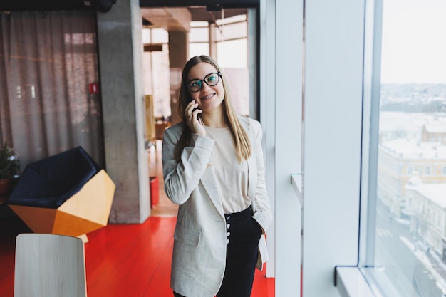 Jolie femme tenant un gadget de smartphone moderne dans ses mains, l'air pensif et rêvant, tenant un téléphone portable, réfléchit à une idée de publication sur les réseaux sociaux