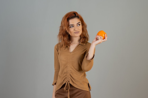 Jolie femme tenant une orange fraîche et regardant loin.