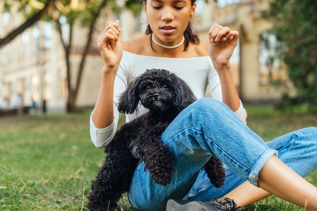 Jolie femme en tenue décontractée assise sur l'herbe dans le parc avec un mignon petit chien