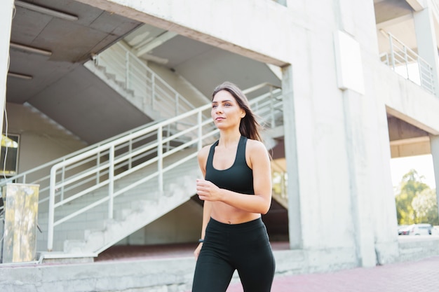 Jolie femme en tenue de sport en cours d'exécution à l'extérieur en milieu urbain.