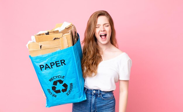 Jolie Femme à Tête Rouge Criant Agressivement, Ayant L'air Très En Colère Et Tenant Un Sac En Papier Recyclé