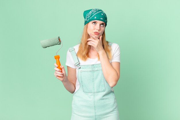 Jolie femme à tête rouge pensant, se sentant douteuse et confuse, concept de maison de peinture