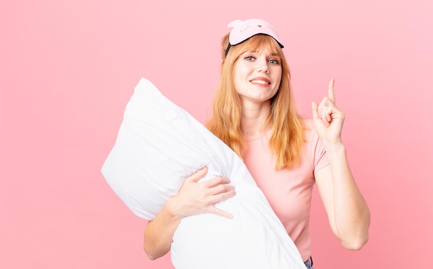 Jolie femme tête rouge en pyjama et tenant un oreiller